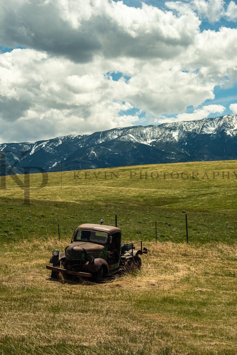 An old rusted truck resting in a pasture beneath mountain clouds.