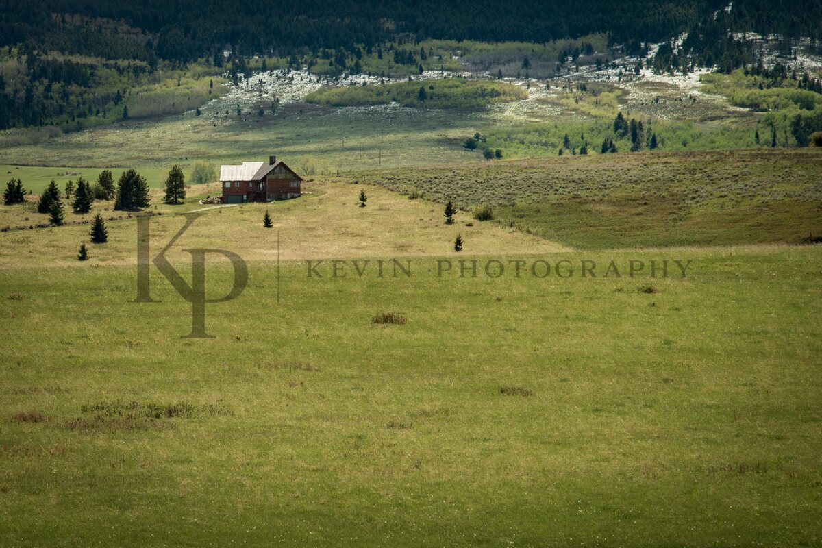 A small ranch house sitting in a wide meadow with valley light beyond.